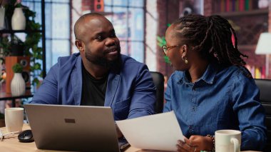 Siyahi insanların her ikisi de görev yönetimi için bilgisayarlarında online araçlar kullanarak belirlenen ofislerinde çalışırlar. Konforlu evlerinden işlemleri verimli bir şekilde tamamlıyorlar. Kamera B.