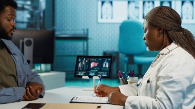 Sağlık görevlisi, genç bir adamın rutin kontrolleri sırasında notlar alıyor, sağlık kayıtlarını inceliyor ve hastalıkların önlenmesi için en iyi tedaviyi öneriyor. Tıp endüstrisi. Kamera A.