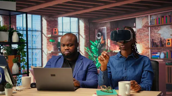 Siyahlar, VR ve Al 'ı günlük iş rutinlerine entegre ederler. Adamın üç boyutlu deneyimi vardır. Genç odaklı kadın, metaevren içindeki kulaklıkla yapılan animasyonu inceliyor. Kamera A.