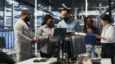 Sunucu odasında gülümseyen mühendislik ekibi altyapı tanılarını inceliyor. Veri merkezinde çalışan bilişim uzmanları, sistem bütünlüğünü ve çalışma saatlerini korumak için performans verilerini analiz ediyorlar. Kamera A