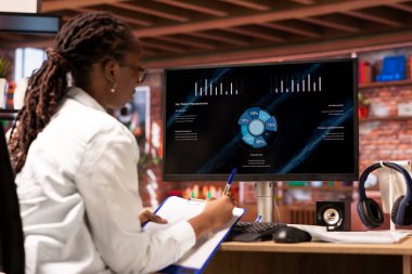 Finansal şirketlerin büyüme grafiklerini dairedeki bilgisayar ekranında gösteren bir telgraf işçisi. Bilgisayardaki satış istatistiklerine bakan kadın gelir rakamlarını gösteriyor, notlar alıyor