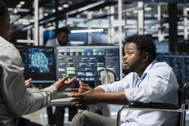 Engelli mühendis ve yönetici makine öğrenimi için kullanılan sinirsel ağ veri merkezini inceliyor. Tekerlekli sandalyedeki ekip lideri ve işçi sunucu merkezini yapay zeka için optimize ediyor.