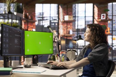 Ofisteki verimliliği arttırmak için yeşil ekranın yanında yapay zeka destekli yazılım kullanan serbest çalışan bir kadın. Sanal asistan, otomasyon ve makine öğreniminin günlük görevleri nasıl dönüştürdüğünü gösterir.