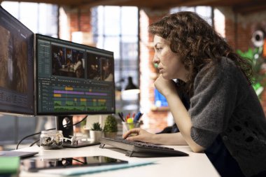 Odaklanmış editör kadın ajans ofisinde, dijital medyada yaratıcı bir yazılımda video montajı üzerinde çalışıyor. Çekimleri düzenlemek ve içerik yaratmak için çift monitör kullanan film yapımcısı, prodüksiyon sonrası.