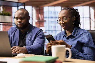 Afrikalı Amerikalı serbest çalışanlar evlerinde bir araştırma projesinde işbirliği yapıyorlar, adam online raporları ve analizleri dizüstü bilgisayarla kullanıyor. Genç kadın cep telefonundan internet yazışmalarını yönetiyor.