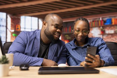 Genç çift, günlük serbest çalışmaya başlamadan önce e-posta kutusunu kontrol ediyor, uzak görevlerin tadını çıkarıyor ve akıllı telefonlarını karıştırıyor. Afrikalı Amerikalıların birbirine tamamen bağlı serbest çalışanları.