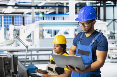 Güneş enerjisi santralindeki fotovoltaik sistemlerde sorun çıkaran Afrikalı Amerikalı uzman dizaynlar için bir PC yazılımı üzerinde çalışıyor. Teknisyen yenilenebilir enerji operasyonlarındaki yapılandırmaları inceliyor.