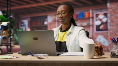 Uzaktan kumandalı bir çalışan, evde kahve içerken, sosyal medya paylaşımlarına bakıyor. Afro-Amerikalı kadın sıcak içecekten zevk alıyor ve laptopta e-kitap okuyor, kamera B