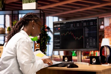 Borsacı hisse senedi alıp satmak için bilgisayar kullanıyor. Kârı maksimuma çıkarmak için doküman dosyalarını karıştırıyor. PC monitöründeki borsa grafiklerine bakan yatırımcı