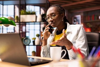 Ofisteki uzaktan kumandalı bir çalışan dizüstü bilgisayarın önünde oturuyor, telefonlara cevap veriyor. İnternette iş yapmak için not defteri kullanan Afrikalı Amerikalı kadın, akıllı telefondan telefon alıyor.