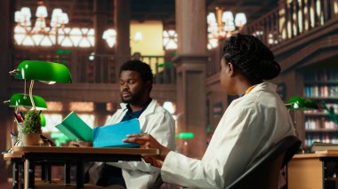 İki tıp fakültesi öğrencisi, izlenim ve fikir alışverişinde bulunarak geleneksel bir kütüphanede çalışmalarına odaklanıyor. Öğrenciler tıbba ve sağlık hizmetlerine büyük bağlılıklarını gösteriyorlar. Kamera B.