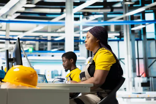 Güneş paneli fabrikasında bilgisayar verileri üreten teknisyen gözlemcileri, verimli güneş enerjisi üretimini desteklemek için çalışan ince unes ekipman ayarları. Montaj hattının yanında oturan kadın.