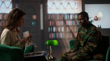 Kadın terapist, danışmanlık oturumunda silahlı kuvvetler üniformalı siyah bir askere Rorschach mürekkep lekesi testi sunuyor. Kitap raflarıyla dolu sıcak bir ofiste terapi gören farklı insanlar. Kamera A.