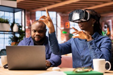 Siyah kız sanal gerçeklikle uğraşırken partneri de masa başında yapay zeka ve interaktif teknolojiyi modern ofis ortamında araştırıyor. Aygıtlarla üç boyutlu simülasyon.