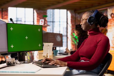 İzole ekran PC kullanarak, müzik dinleyerek başlangıç ofisinde programlayıcı kodlaması. Krom anahtar bilgisayar kullanarak kulaklık takan Afrika kökenli Amerikan yapay zeka endüstrisi teknisyeni