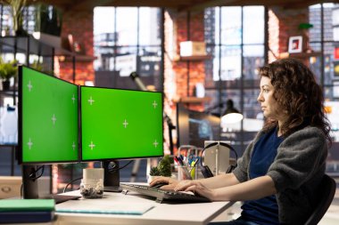 Profesyonel kadın, modern çalışma alanında çift ekran monitörlerde yeşil ekran kullanıyor. Yüksek teknoloji ofis ortamı üretkenliği artırıyor, bilişim uzmanları ve içerik oluşturulması için ideal.