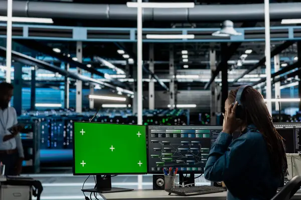 Sunucu odası çalışanı, ses kulaklığı takıyor. Model bilgisayar kullanarak bakım yapıyor. Veri merkezinde ekipman performansını kontrol etmek ve müzik dinlemek için yeşil ekran bilgisayar kullanan teknisyen