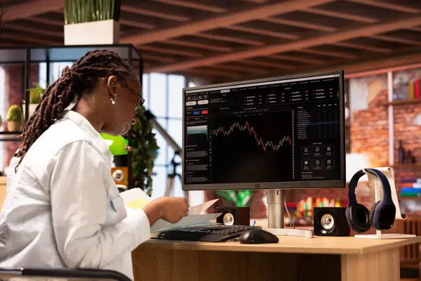 Hisse senedi alıp satmak, dosya okumak, piyasa eğilimlerinden ve dalgalanmalardan yararlanmak için bilgisayar kullanan bir kadın. Yatırımcı bilgisayar monitöründe hisse senedi önizlemesi eğilimleri, belgelere bakıyor