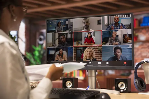 İş arkadaşlarıyla görüntülü görüşme yapan, evrakları sunan bir telgraf işçisi. Ekip telekonferansına katılan uzaktan çalışan birden fazla katılımcıyla birlikte dosyaları inceliyor.