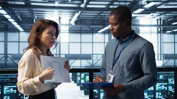 Veri merkezi ekibi yüksek teknoloji sunucu odasındaki evrak dosyalarını inceliyor. Kritik sistem raporlarını ve güvenlik protokollerini inceliyor. Mali belgelere bakan sunucu odası yöneticileri, kamera B