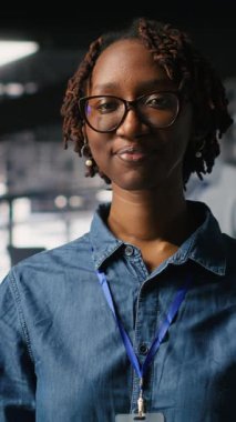 Sunucu merkezi mühendisliği ekibinin yanındaki dikey video teknisyeni yapay zeka teşhislerini inceliyor. Operasyonel güvenilirliği korumak için veri merkezinde çalışan neşeli Afrikalı Amerikalı kadın.