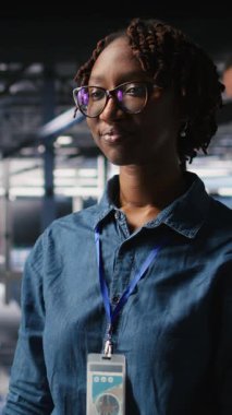 Sunucu merkezi mühendisliği ekibinin yanındaki dikey video teknisyeni yapay zeka teşhislerini inceliyor. Operasyonel güvenilirliği korumak için veri merkezinde çalışan neşeli Afrikalı Amerikalı kadın.