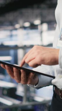 Sunucu odası çalışanının dikey videosu AI LLM görselleştirmesini inceleyen meslektaşının yanındaki tablet üzerindeki kodu kontrol ediyor. Yapay zeka sistemlerini izlemek için aygıt kullanan veri merkezi bilişim uzmanı