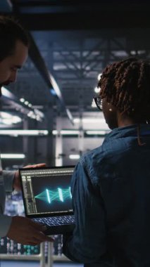 Dikey video sunucusu çiftlik yöneticisi nöral ağ kodunu ve LLM görselleştirme panellerini inceleyen mühendis tarafından yapılan çalışmaları denetliyor. Ekip lideri AI sistem performansını izleyen işçi denetliyor