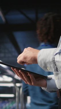 Sunucu odası çalışanının dikey videosu AI LLM görselleştirmesini inceleyen meslektaşının yanındaki tablet üzerindeki kodu kontrol ediyor. Yapay zeka sistemlerini izlemek için aygıt kullanan veri merkezi bilişim uzmanı