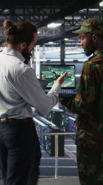 Veritabanındaki dikey video uzmanları İHA gözetleme görüntülerini dizüstü bilgisayardan inceliyor. Ordu birimleri yüksek teknoloji sunucu odasında defter kullanarak savaş alanı keşif operasyonları yapıyor.