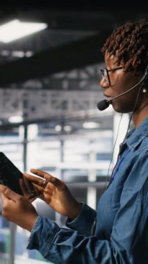 Dikey video sunucusu merkezi bilişim uzmanı sistemlerini izliyor, teknik destek veriyor, sorun çözme aşamalarında kullanıcılara rehberlik ediyor. Afrika kökenli Amerikalı teknisyen mikrofon kullanarak uzaktan tanı koyuyor.