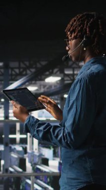 Dikey video sunucusu merkezi bilişim uzmanı sistemlerini izliyor, teknik destek veriyor, sorun çözme aşamalarında kullanıcılara rehberlik ediyor. Afrika kökenli Amerikalı teknisyen mikrofon kullanarak uzaktan tanı koyuyor.