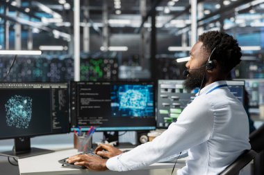 Kulaklık mikrofonuyla konuşan bir çalışan. Yapay zekayı çalıştırmak için gerekli veri merkezini kuran teknisyenlerle konuşuyor. Yapay zeka araçları yükleyen mühendislerle birlikte sunucu odası çalışanı