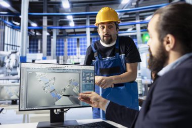 Fotovoltaik fabrikasının müdürü işçiyle konuşuyor, arızalı sistemleri teşhis ediyor, bilgisayar ekranına işaret ediyor. Güneş panelleri fabrika uzmanları dinlenme süresini azaltmak için beyin fırtınası yapıyor.