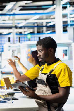 Fotovoltaik fabrikasındaki Afrikalı Amerikalı teknisyen üretim hattı sistemlerini teşhis etmek için tabletle hata ayıklama yapıyor. Güneş panelleri fabrika işçisi çalışma süresini azaltıyor, üretim bandı üretiyor.