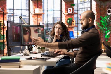 Grafik tasarımcı ve fotoğrafçı, bir PC üzerinde yapay zeka destekli fotoğraf düzenleme yazılımı kullanarak modern bir stüdyoda işbirliği yapmaktadır. Otomasyon, rötuş ve gelişmiş görüntü ayarlama araçları sağlanıyor.