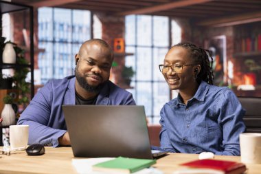 Siyah adam ve kadın rahat dairelerinde oturup dizüstü bilgisayarda dijital pazarlama stratejisini tartışıyorlar. Birbirlerine uzak işlerinde ve serbest yolculuklarında destek oluyorlar..