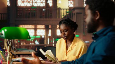 Afrikalı Amerikalı akademisyenler ders notlarını okuyor ve kütüphanedeki bilgileri karşılaştırıyor, akademik veritabanını araştırma için birlikte çalışıyorlar. Eğitici materyaller. Kamera B.