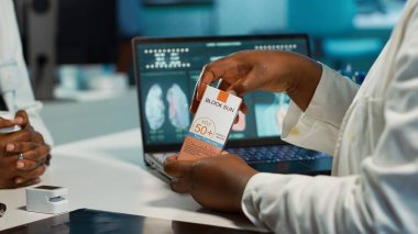 Afrikalı Amerikalı bir kız ultraviyole ışınlı iyi güneş kremi kalkanını soruyor. Doktor cilt bakımı için spf 50 öneriyor. Doktor ve hasta dermatoloji kontrolünde. Kamera A.