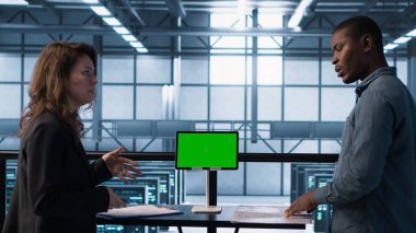 Veri merkezi ekibi yeşil ekran tableti kullanıyor evrak dosyalarını ve güvenlik protokollerini inceliyor. Kritik sistem raporlarını analiz eden kroma anahtar cihazının yanındaki sunucu odası adresleri, kamera A