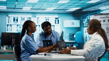 Kabinede bir sağlık ekibine liderlik eden Afrikalı Amerikalı pratisyen, MRI görüntüleme sonuçlarını analiz ediyor ve doğru teşhis ve etkili tedavi sağlıyor. Tıbbi tesis. Kamera B.