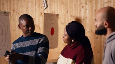 Atış poligonu eğitmeni müşterilere nasıl silah doldurulacağını ve nasıl tutulacağını gösteriyor. Menzil aktivitelerini denetliyor. Atış poligonu uzmanı silah adabı öğretiyor, kamera B