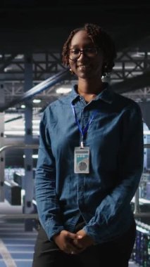 Hataları tespit etmek için ekipman kontrolü yapan iş arkadaşlarının yanında gülümseyen veri merkezi yöneticisinin dikey video portresi. Bilgi işlem uzmanlarının yanındaki mutlu kadın başarısızlığı önlemek ve en aza indirmek için çalışıyor