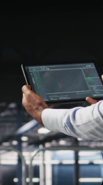 Tablet üzerinde çalışan kod ayıklama araçlarına bakan veri merkezi programcısının dikey videosu. Sunucu çiftliği IT profesyonel kontrol makinesi öğrenme betiği otomatik görevleri, kamera A