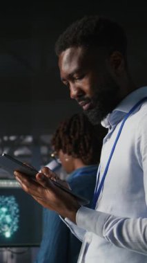 Veri merkezi endüstriyel platformunda yürüyen dikey video mühendisi sistem bakımını yapıyor. BT uzmanı, güncelleme yapmak, hataları çözmek ve altyapı istikrarını artırmak için tablet kullanıyor