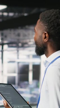 Dikey video veri merkezi programcısı kod satırlarını kontrol ediyor ve iş arkadaşı AI LLM görselleştirmelerini inceliyor. Bilişim uzmanları, istikrarlı altyapı operasyonlarını sağlamak için nöral ağ çıktılarını analiz ederler