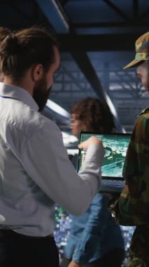 Veri merkezindeki dikey video operatörleri İHA kontrol yazılımını çalıştırmak için dizüstü bilgisayar kullanarak görev haritasına bakıyorlar. Askeri uzmanlar otonom hava araçlarının stratejik konuşlandırılmasını yapıyorlar