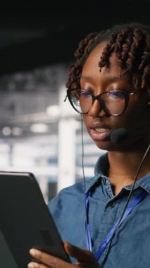 Kulaklık takan dikey video veri merkezi mühendisi tablet kullanarak uzaktan tanı koyuyor. Teknisyen sistem sağlığını izliyor ve kullanıcılara altyapı sorunları çözmede rehberlik ediyor