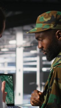 Veritabanındaki dikey video uzmanları İHA gözetleme görüntülerini dizüstü bilgisayardan inceliyor. Ordu birimleri yüksek teknoloji sunucu odasında defter kullanarak savaş alanı keşif operasyonları yapıyor.