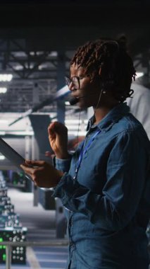 Tablet ve kulaklık kullanarak altyapı teknik desteği sağlayan dikey video sunucu odası yönetimi. Veri merkezi bilişim uzmanı uzak ekiplerle koordine ederken arka uç sorunlarını çözer